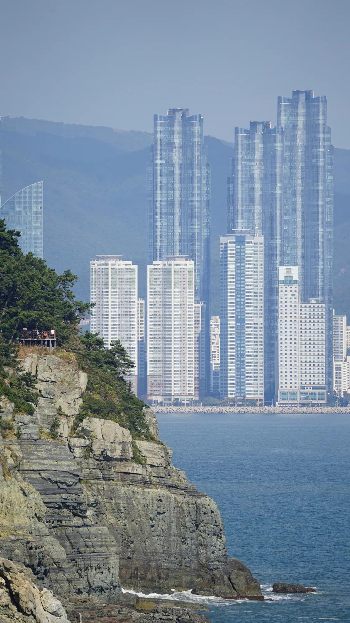 Rocky coastline in front of high-rise buildings and wooded hills in Busan