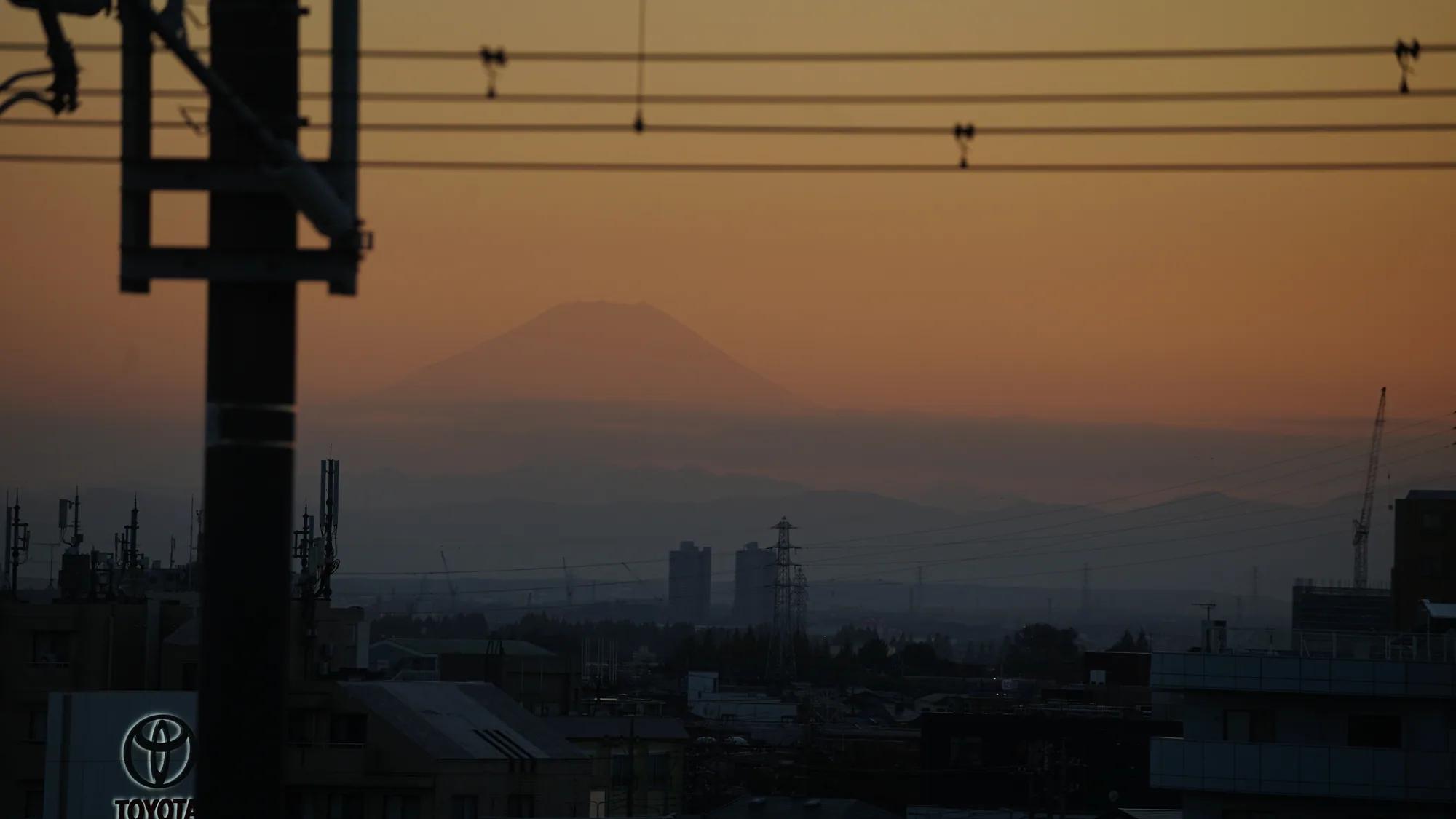 Silhouette of Mount Fuji beyond railway lines in orange evening light