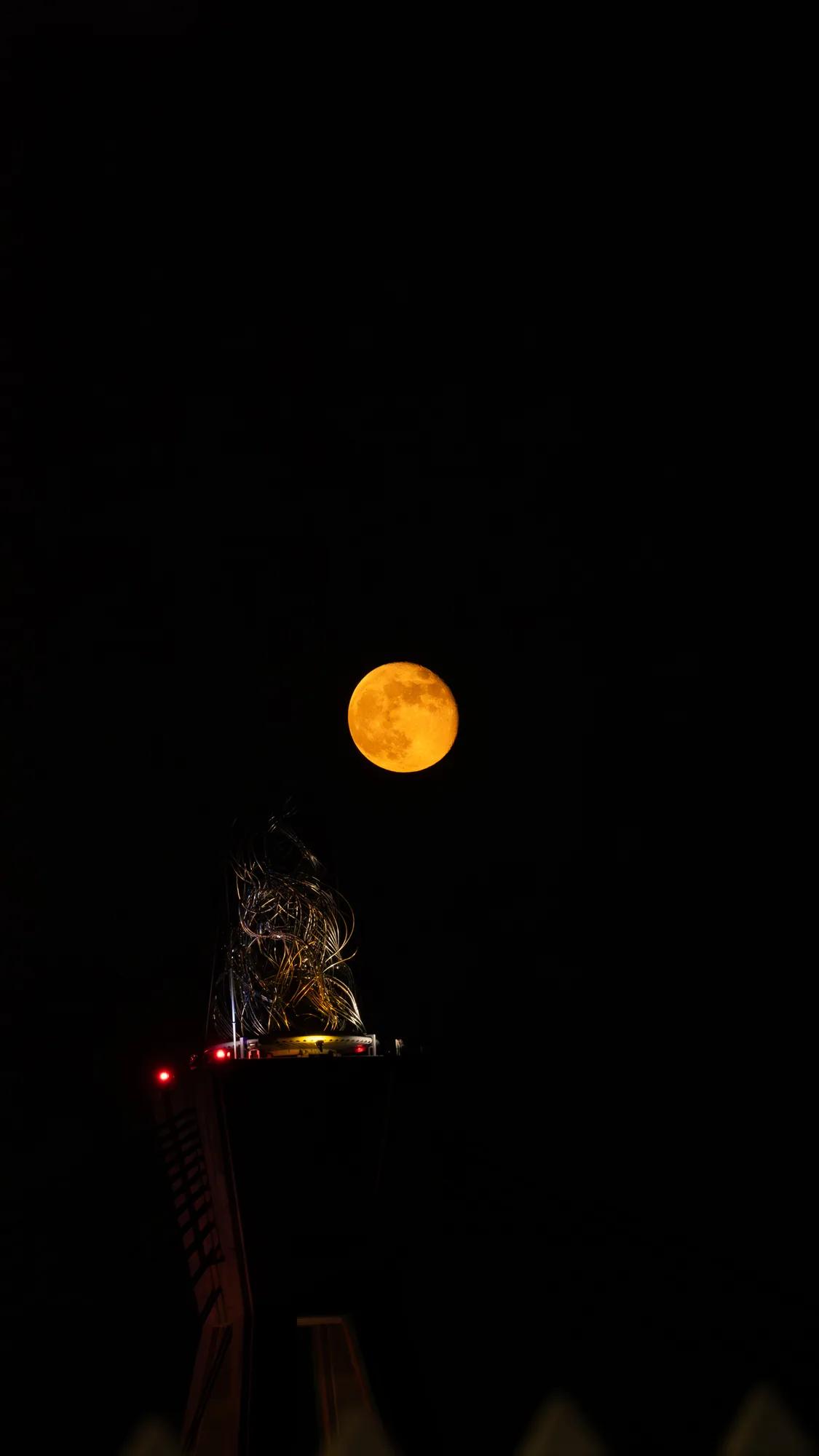 Orange moon above the top of an illuminated tower