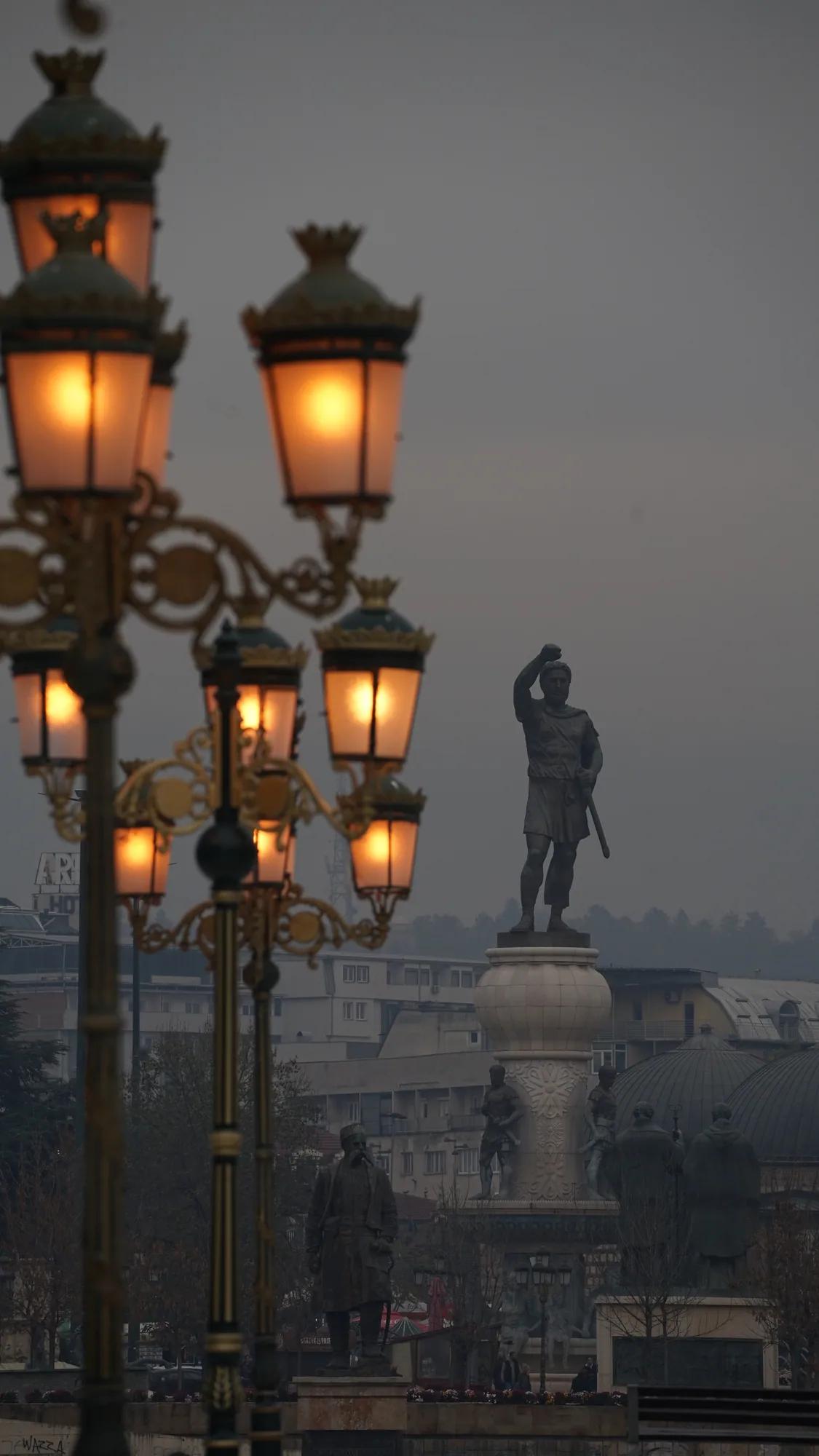 Glowing historic lanterns and a monument in dense fog in Skopje