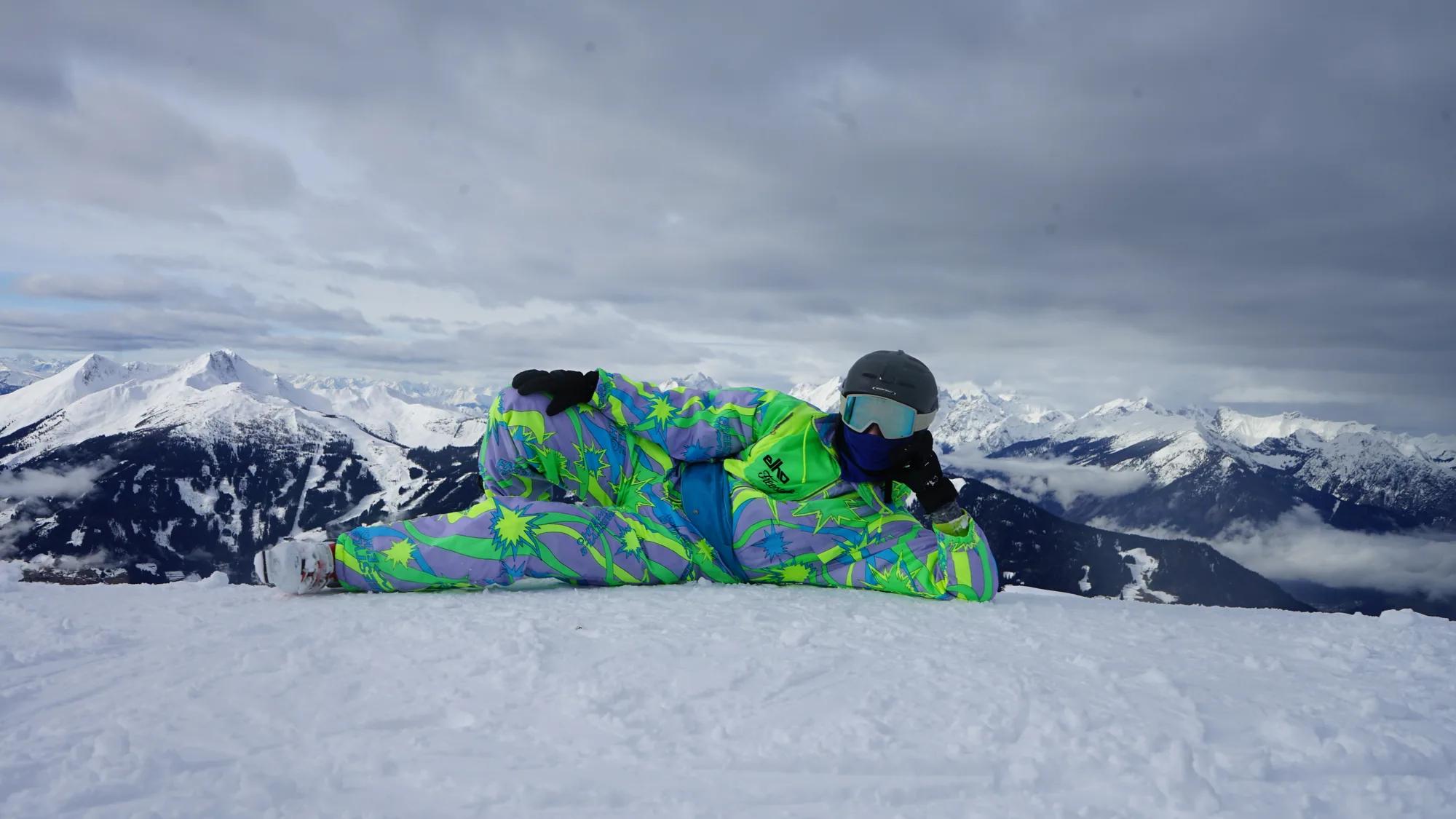 Person in a colourful snowsuit posing in front of a wintry mountain panorama