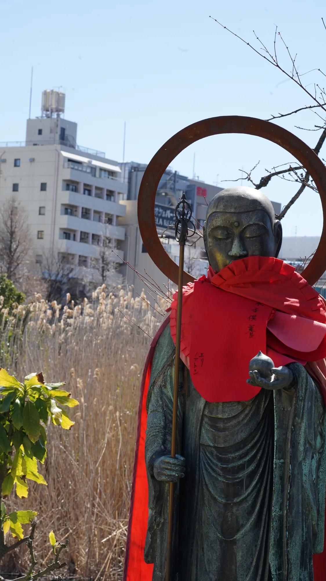 Jizo statue with red bibs in front of city buildings in Tokyo